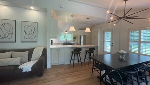 Una cocina moderna con armarios blancos, una isla central con taburetes, iluminación colgante y una mesa de comedor con sillas.