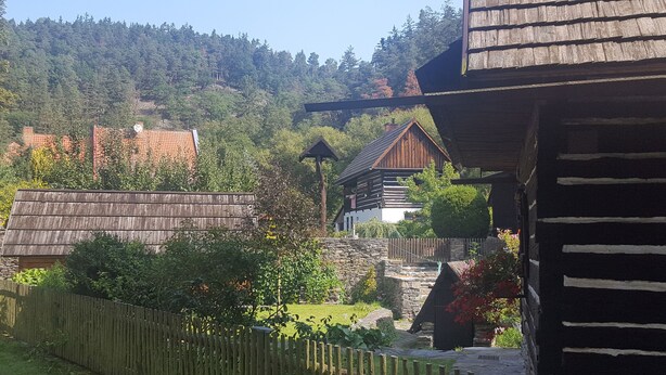A rustic wooden building with a stone staircase leading to a wooden deck, surrounded by greenery and a forested hillside. - Terrace with gorgeous panorama in historic Rabstejn (Manetín)