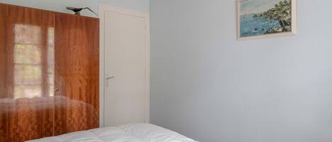 A bedroom with a wooden wardrobe, a white door, and a painting of a coastal scene.