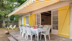 An outdoor dining area with a stone-paved patio, a table set with chairs, and a striped awning. - House between pine trees and beach (Saint-Brevin-les-Pins)