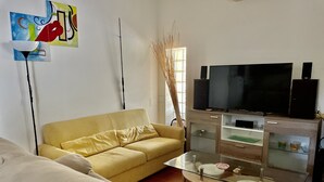 A living room with a yellow sofa, a glass coffee table, a TV on a wooden cabinet, and abstract art on the wall. - Sabaudia Holiday home Il Maestrale (Lazio)