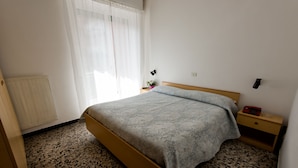 Un dormitorio con cama, mesita de noche, lámpara, radiador y ventana con cortinas.