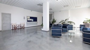 Un vestíbulo amplio con techo alto, un mostrador de recepción, una zona de estar con asientos azules y una puerta.