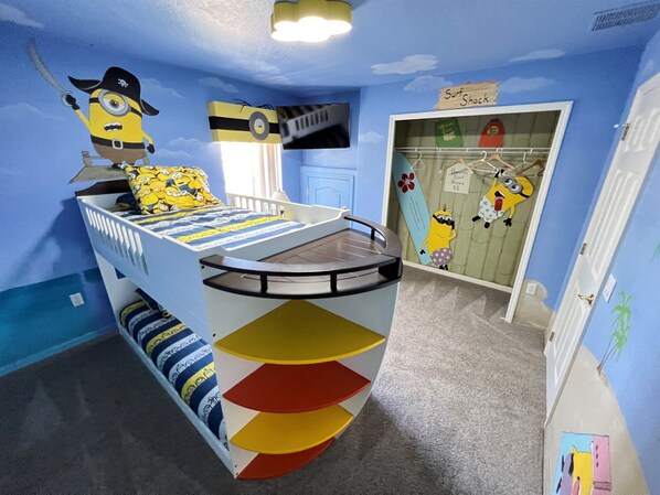 A child's bedroom with a bunk bed, a Minion-themed bedspread, a surfboard decoration, and a closet with Minion stickers.