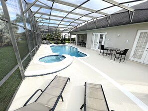 A covered outdoor swimming pool with lounge chairs and a table.
