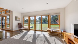 A spacious living room with large sliding glass doors, a comfortable chair, a wooden coffee table, and a flat-screen TV. - Punka River Retreat - Porepunkah, Victoria (Porepunkah)