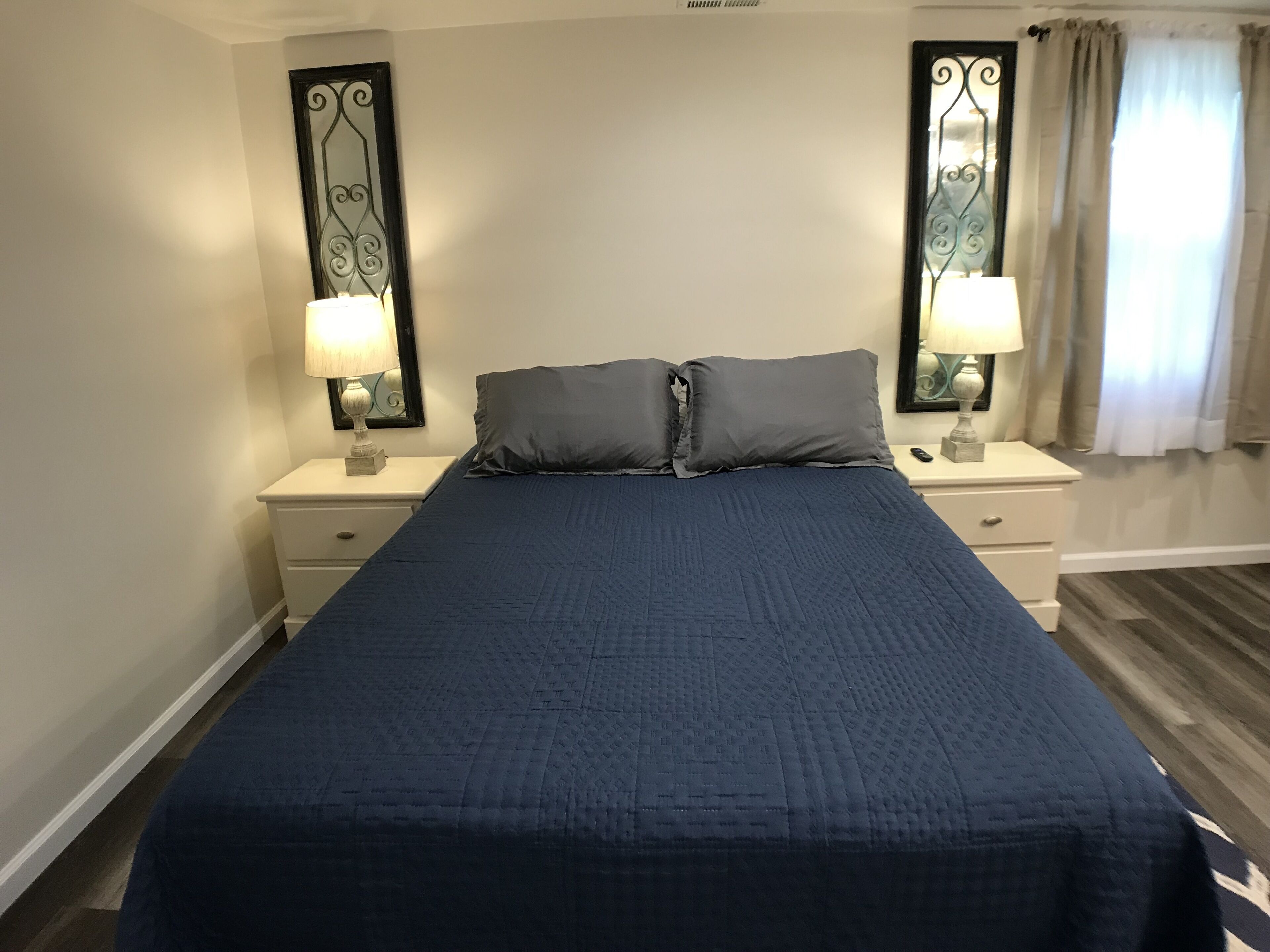 A neatly made bed with a blue quilt, two bedside tables with lamps, and a mirror with a decorative frame.