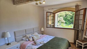 Un dormitorio con cama, mesita de noche, lámpara y ventana con vistas al verdor.