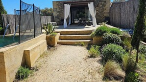 Un patio trasero con piscina, una construcción de piedra y una cerca de madera.