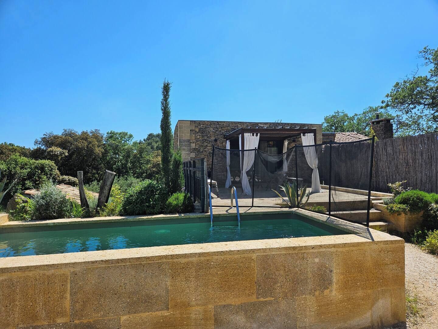 A pool area with a stone border, a covered seating area, and a stone building in the background.