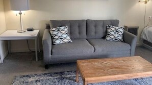 A living room with a grey sofa, two patterned throw pillows, a wooden coffee table, a lamp, and a painting on the wall. - 4302  Hot tub, sauna & more resort amenities  Grandfather View @ Pinnacle (Beech Mountain)