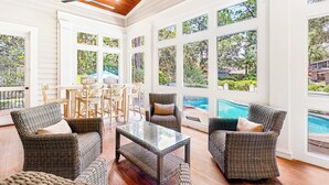 A sunlit room with wicker furniture, large windows, and a ceiling fan.