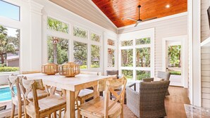 A spacious room with a wooden ceiling, large windows, a pool, and wicker furniture.