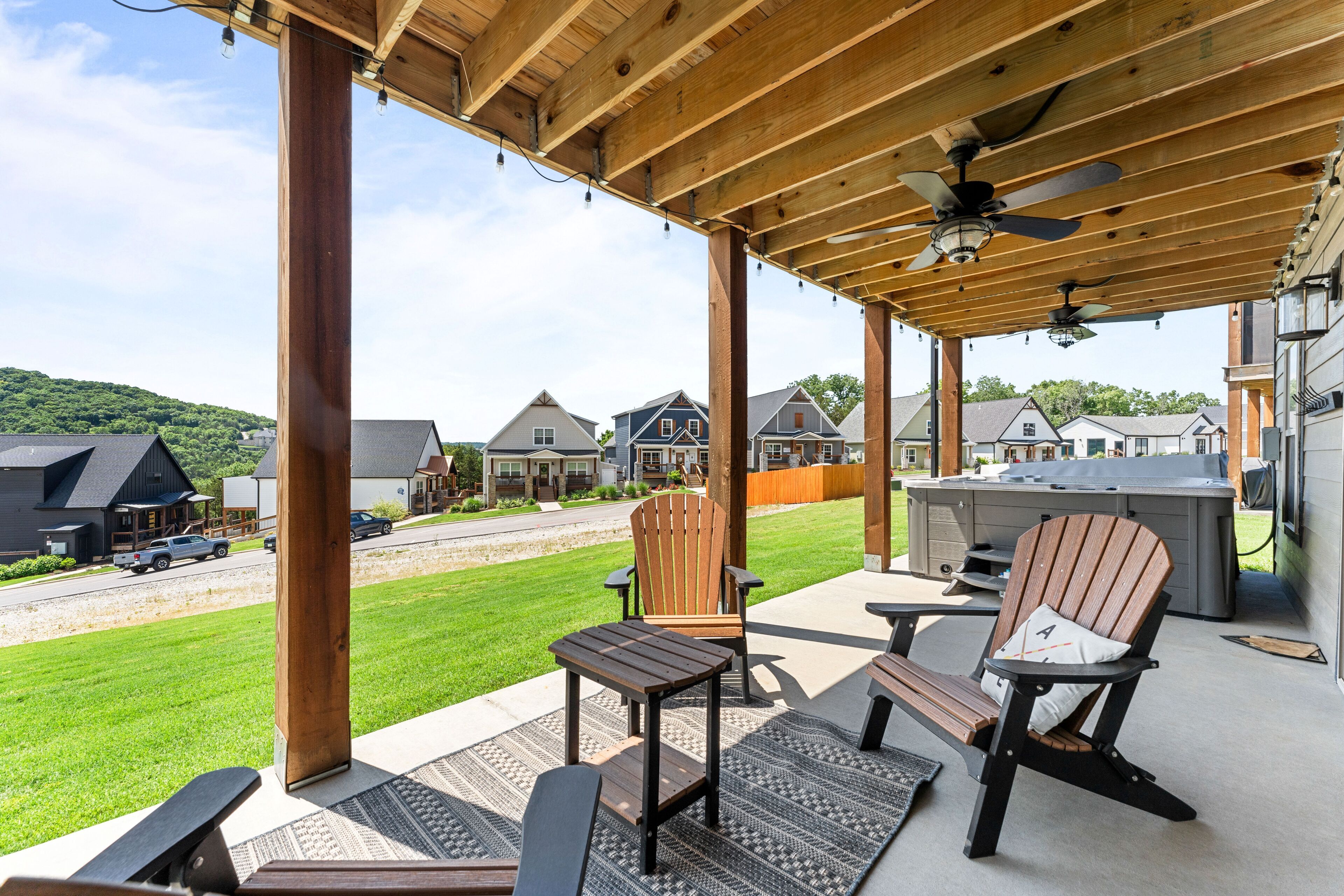 A covered patio with wooden chairs and a table, a hot tub, and a view of a residential area.