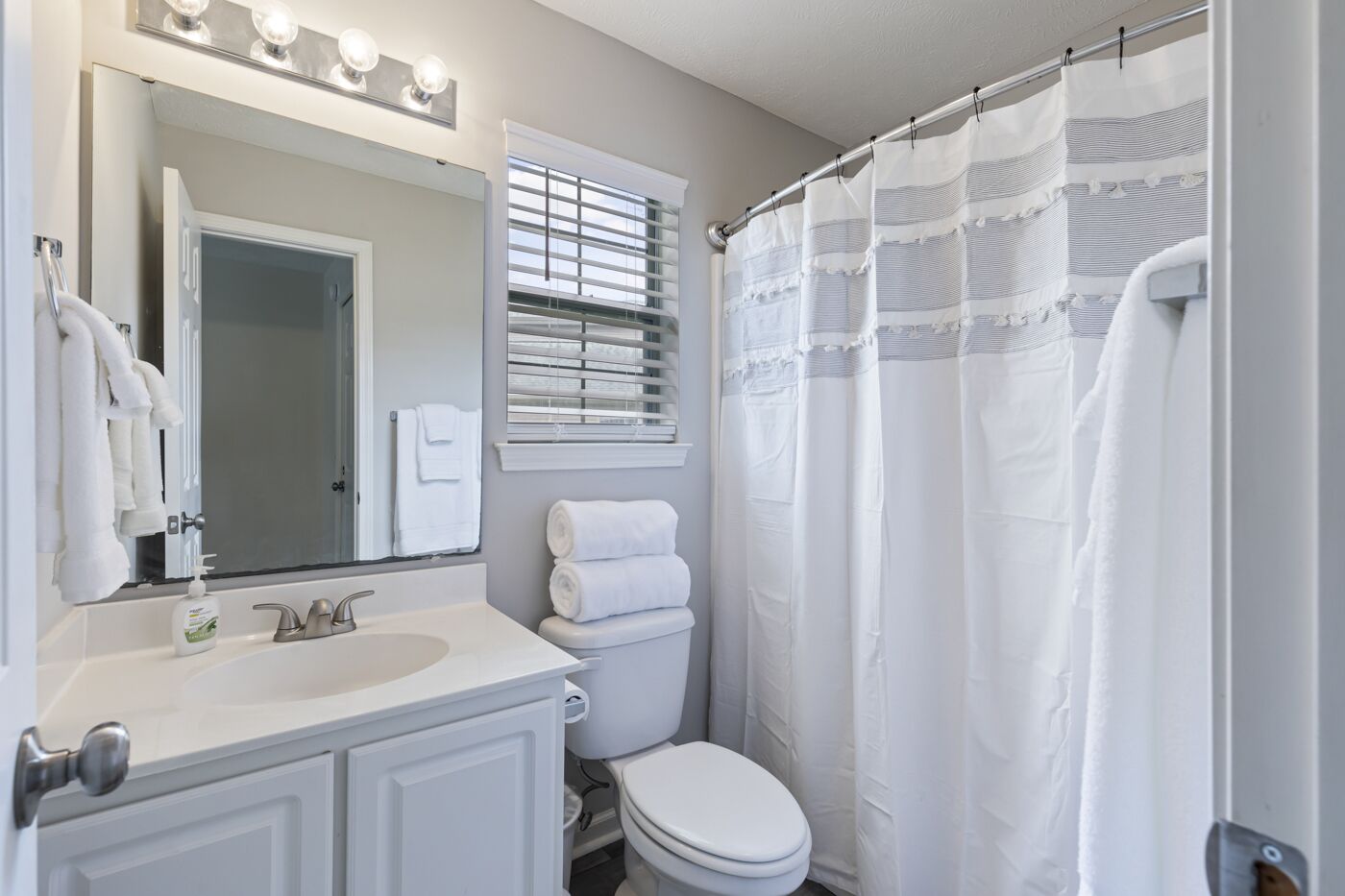 Une salle de bain avec un lavabo blanc, un miroir et des toilettes. Des serviettes sont accrochées au mur et il y a un rideau de douche.