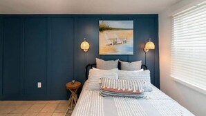 A bedroom with a bed, a nightstand, a painting, and two wall-mounted lamps.