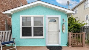 A small, single-story house with a turquoise exterior, a white door, and a window with blinds.