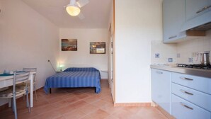 Een kleine kamer met een bed, een bureau en een kitchenette.