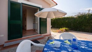 Een terras met een tafel gedekt voor twee personen, een open deur en een witte parasol.