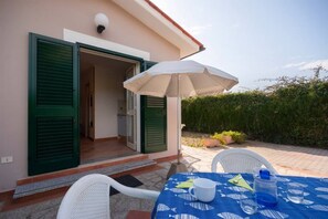 A patio with a table set for two, an open door, and a white umbrella.