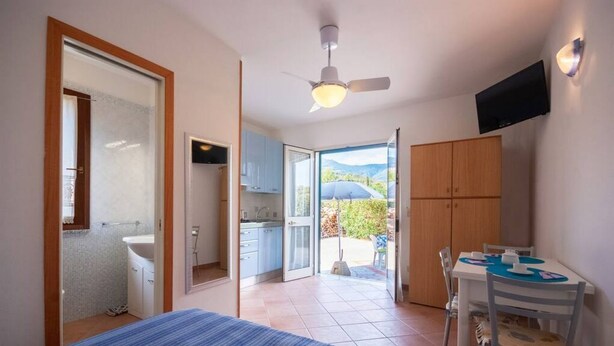 Een slaapkamer met een bed, een plafondventilator, een televisie en uitzicht op een balkon met een tafel en stoelen.