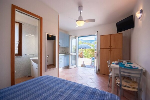 A bedroom with a bed, a ceiling fan, a TV, and a view of a balcony with a table and chairs.