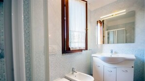 Een badkamer met toilet, bidet, wastafel en spiegel.