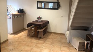 Ein kleiner Essbereich mit einem Holztisch und Bänken, im Hintergrund eine Küche und eine Treppe rechts.