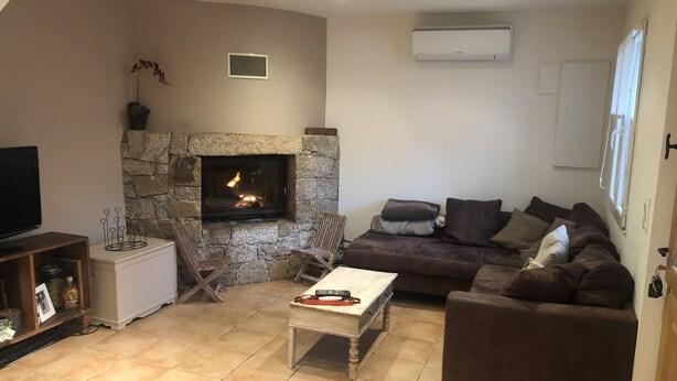 Ein Wohnzimmer mit Kamin aus Stein, einem braunen Sofa, einem Holztisch und einem Fernseher auf einem Schrank.