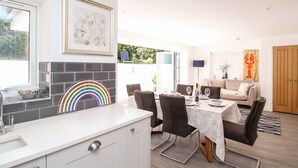 A modern kitchen with a white countertop, a rainbow-shaped light fixture, and a dining area with a table set for four.