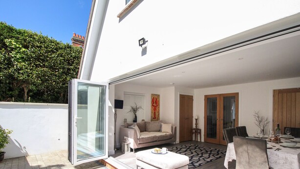 An open-plan living area with a sofa, dining table, and chairs, a sliding glass door leading to a patio, and a small side table with a lamp.