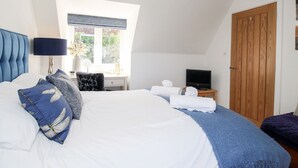 A bedroom with a large bed, a desk with a computer, a television, and a wooden door.