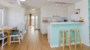 A modern kitchen with white cabinets, a teal accent wall, and wooden stools. - Beautiful 1 BR Condo Overlooking Freeman Park (Carolina Beach)