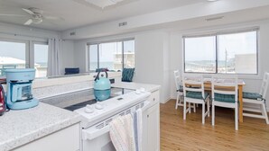 A modern kitchen with a coffee maker, kettle, and dining area with chairs and a table. - Beautiful 1 BR Condo Overlooking Freeman Park (Carolina Beach)