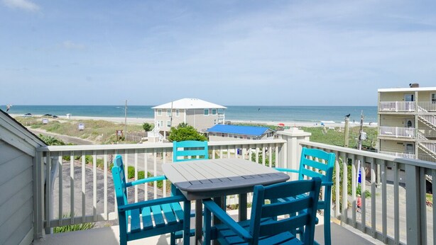 A balcony with a table and chairs overlooking a beach. - Beautiful 1 BR Condo Overlooking Freeman Park (Carolina Beach)