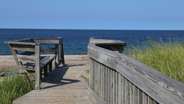 A wooden boardwalk leading to beach chairs and a railing overlooking the ocean. - Sparkling home in quiet private beach community (Sandwich)