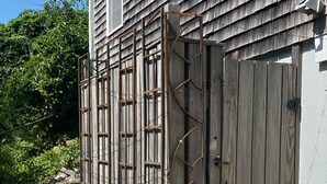 A wooden gate with a metal frame, leading to a house with a shingled roof. - Sparkling home in quiet private beach community (Sandwich)
