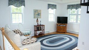 A living room with a sofa, a chair, a TV stand, and a rug. - Sparkling home in quiet private beach community (Sandwich)