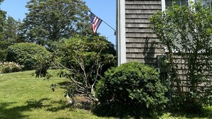 A house with a gray shingled exterior, a white window, and an American flag. - Sparkling home in quiet private beach community (Sandwich)