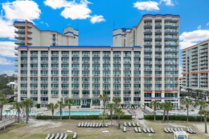 A multi-story hotel with a pool area, palm trees, and sun loungers. - Dunes Village by Elliott Beach Rentals (Myrtle Beach)