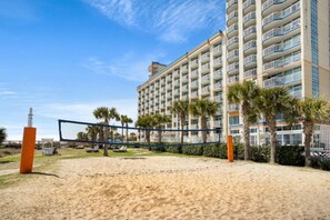 A beach volleyball court with a net, palm trees, and a hotel building in the background. - Dunes Village by Elliott Beach Rentals (Myrtle Beach)
