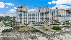 A large hotel with multiple floors, a central courtyard, and a beach area with sun loungers. - Dunes Village by Elliott Beach Rentals (Myrtle Beach)
