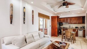 A living room with a sofa, coffee table, and decorative items. There is a dining area with a table and chairs. The kitchen has wooden cabinets and modern appliances. - Matapalo 602, romantic, luxurious, 2 BR apt. with stunning views (Tamarindo)