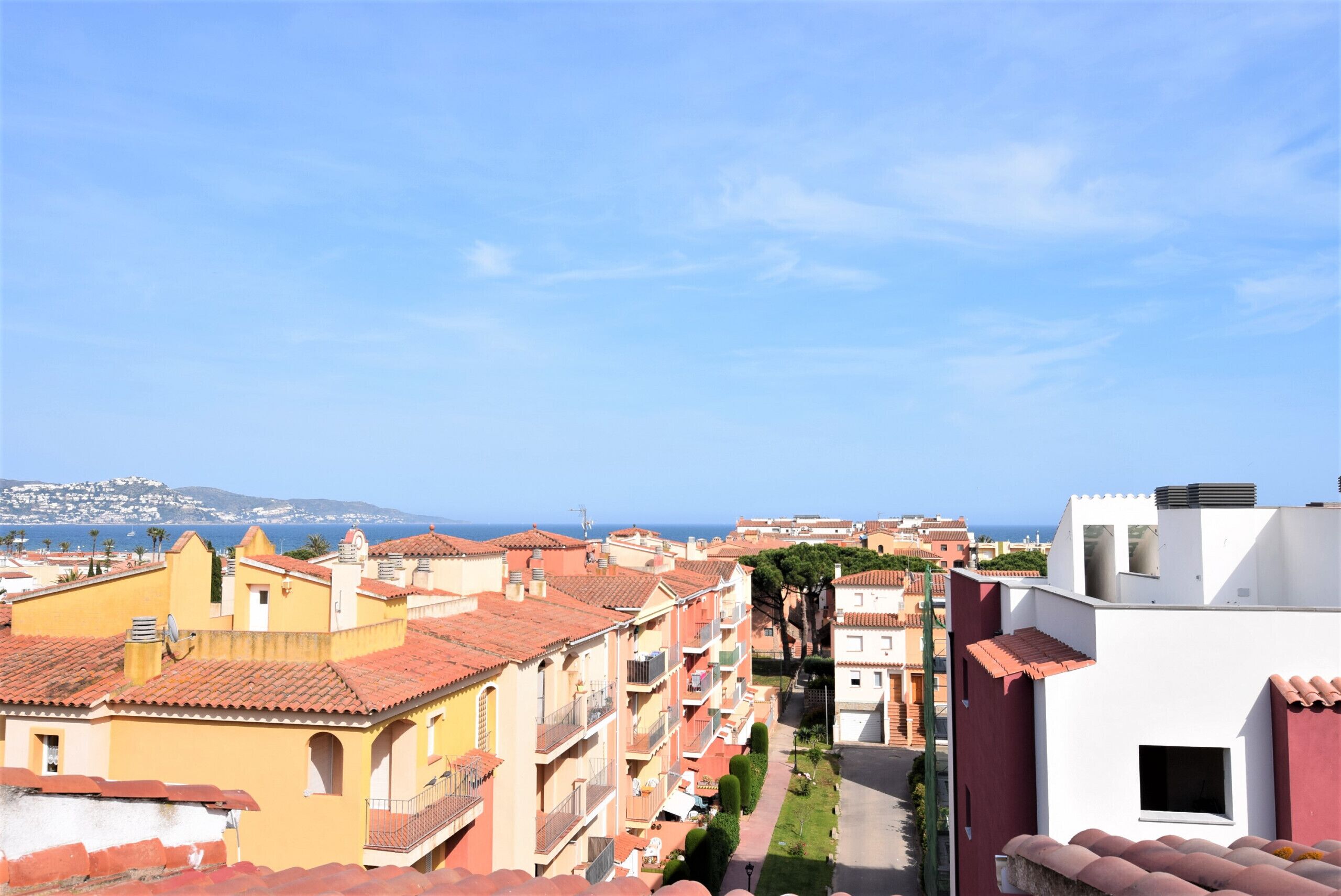 Eine Küstenwohngegend mit Häusern mit Terrakotta-Dächern, einem wolkenlosen Himmel und Blick auf das Meer.