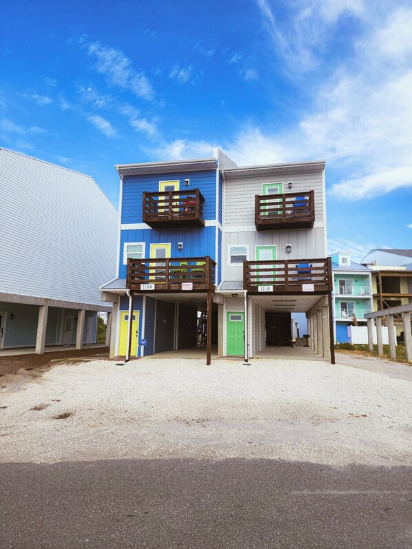 A two-story building with balconies, a covered entrance, and a gravel driveway.