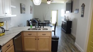 A kitchen with wooden cabinets, a sink, and a dining area with a table and chairs. - ~No Bad Days Townhome~ - 300ft to the sand! (Mexico Beach)