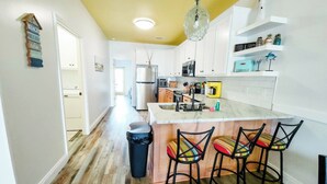 A kitchen with a central island, bar stools, a trash bin, and a hanging light fixture. - ~No Bad Days Townhome~ - 300ft to the sand! (Mexico Beach)