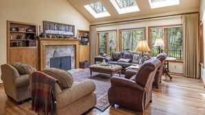 A spacious living room with a fireplace, comfortable seating, and large windows with natural light.