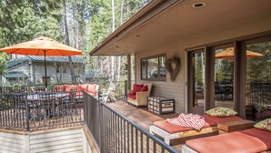 A covered deck with outdoor furniture, a dining area, and a view of the surrounding forest.