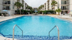 Ein Swimmingpool mit klarem, blauem Wasser, umgeben von einem Gebäude mit Balkonen und Palmen.